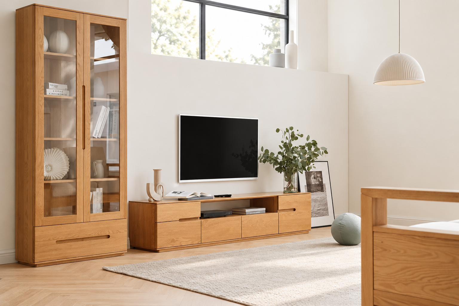 A modern living room featuring a light oak wood TV stand and a matching tall glass-front cabinet, with a wall-mounted TV and neutral-toned decor.