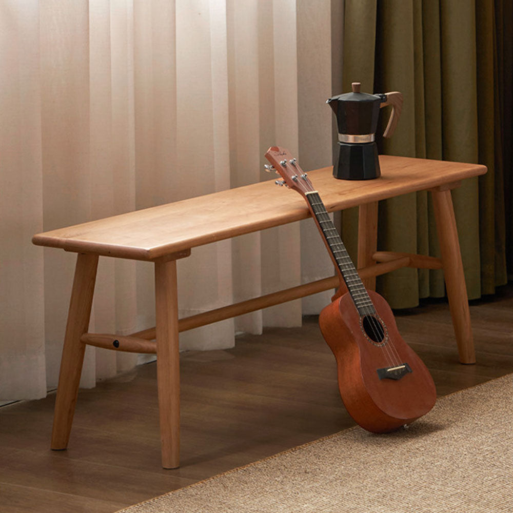 Acuto natural solid cherry dining bench with braced legs, shown beside a dining table as a warm timber bench seat for compact dining spaces