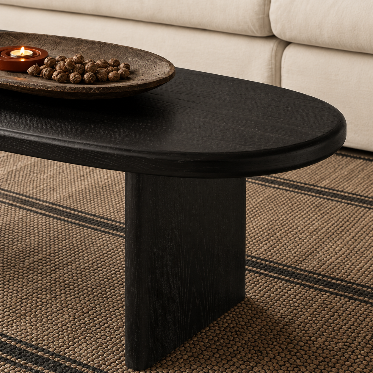 Angled view of a black ash wood oval coffee table with a long rounded tabletop and two solid panel legs.