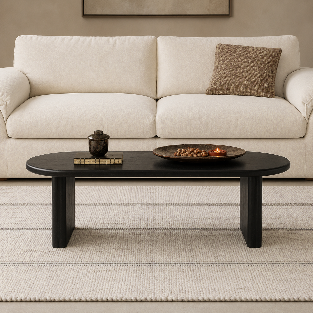 Front view of a black ash wood oval coffee table styled in front of a cream sofa.