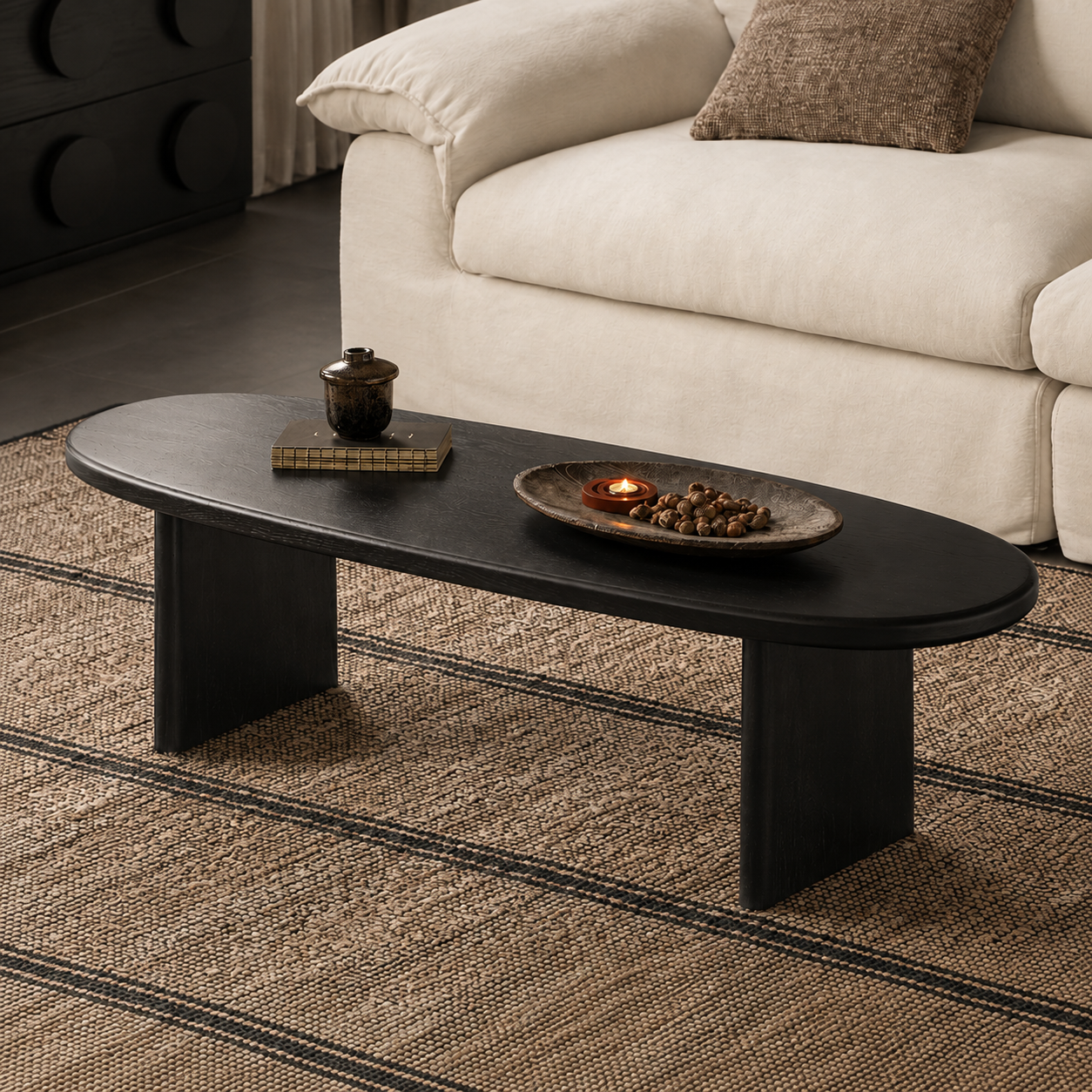 Black ash wood oval coffee table with rounded edges and solid panel legs in a modern living room.