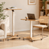 Cary natural solid oak movable small desk shown at sitting and standing heights in a warm living room workspace