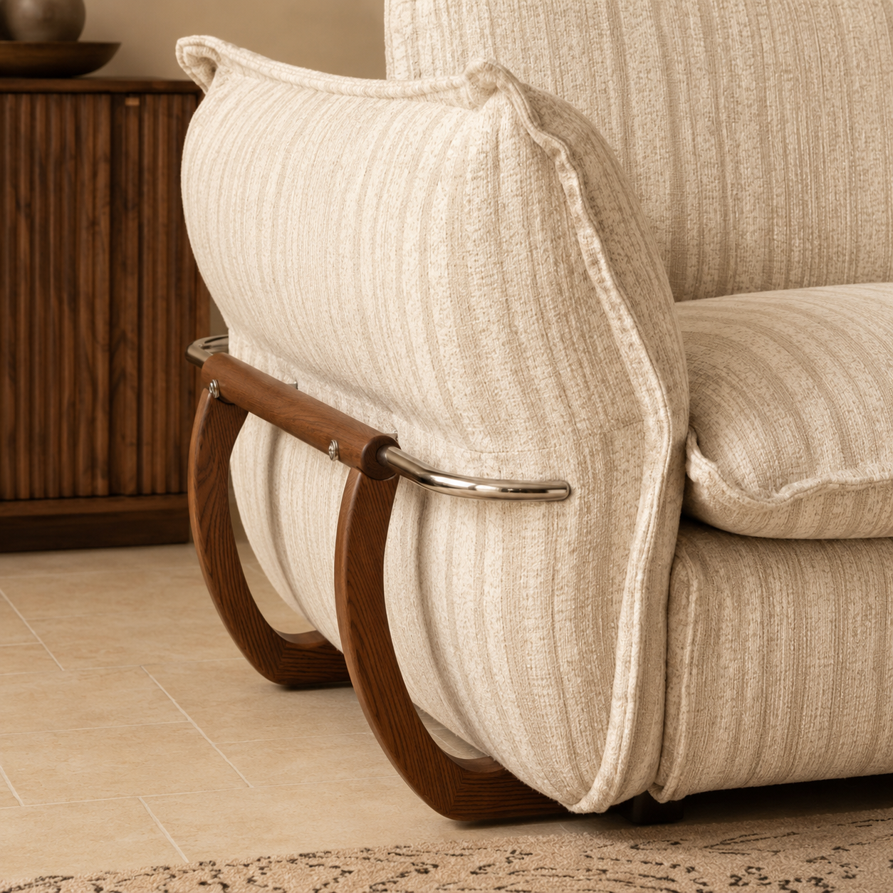 Detailed view of the cream striped sofa arm with soft upholstery, curved wooden frame and polished metal rail.