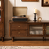 Close-up of a dark wood TV unit featuring drawers, brass hardware and fluted glass cabinet doors.