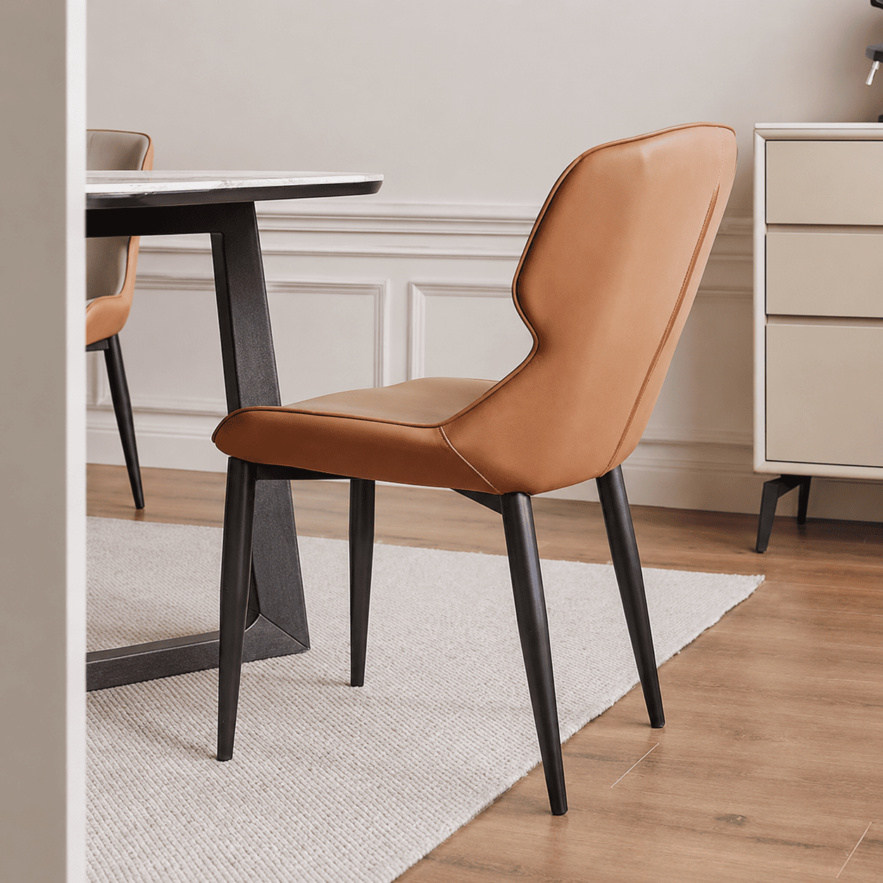 Eden Design Luxe Faux Leather Dining Chair in tan upholstery with slim black legs beside a modern dining table.