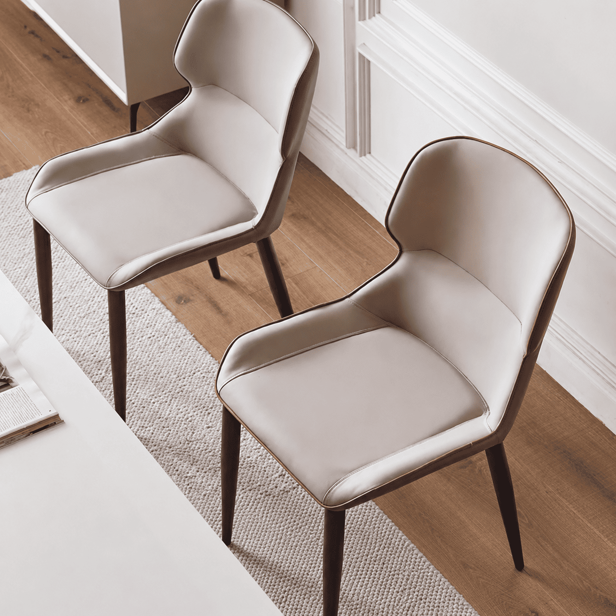 Pair of Eden Design Luxe Faux Leather Dining Chairs with cream seats, brown outer backs, and tapered legs in a bright dining room.