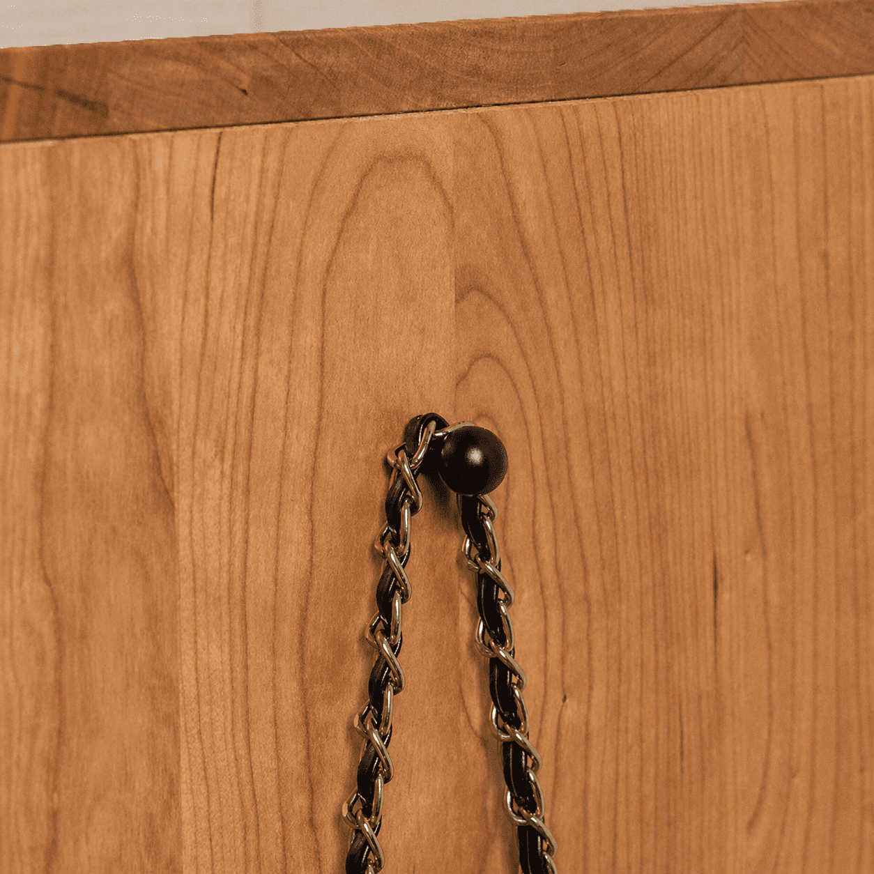 Enna Natural Solid Cherry Shoe Cabinet close-up showing warm cherry wood grain, black wall hook, and safety chain detail.
