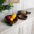 Dark wooden fruit trays in assorted rounded shapes displayed with fresh fruit