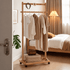Fukuoka natural solid oak movable coat rack with neutral clothing and storage basket beside bed