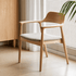Graz Natural Solid Ash Dining Chair with curved wooden arms, grey upholstered seat and natural ash finish beside window blinds
