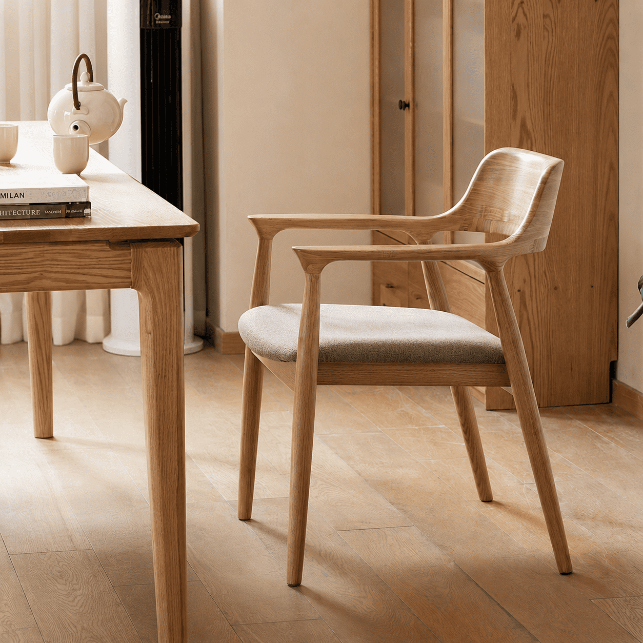 Graz Natural Solid Ash Dining Chair in natural wood finish with tapered legs, rounded armrests and cushioned grey seat beside a dining table