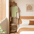 Kent natural solid oak coat rack placed beside a wooden bed with clothes and lower storage shelves