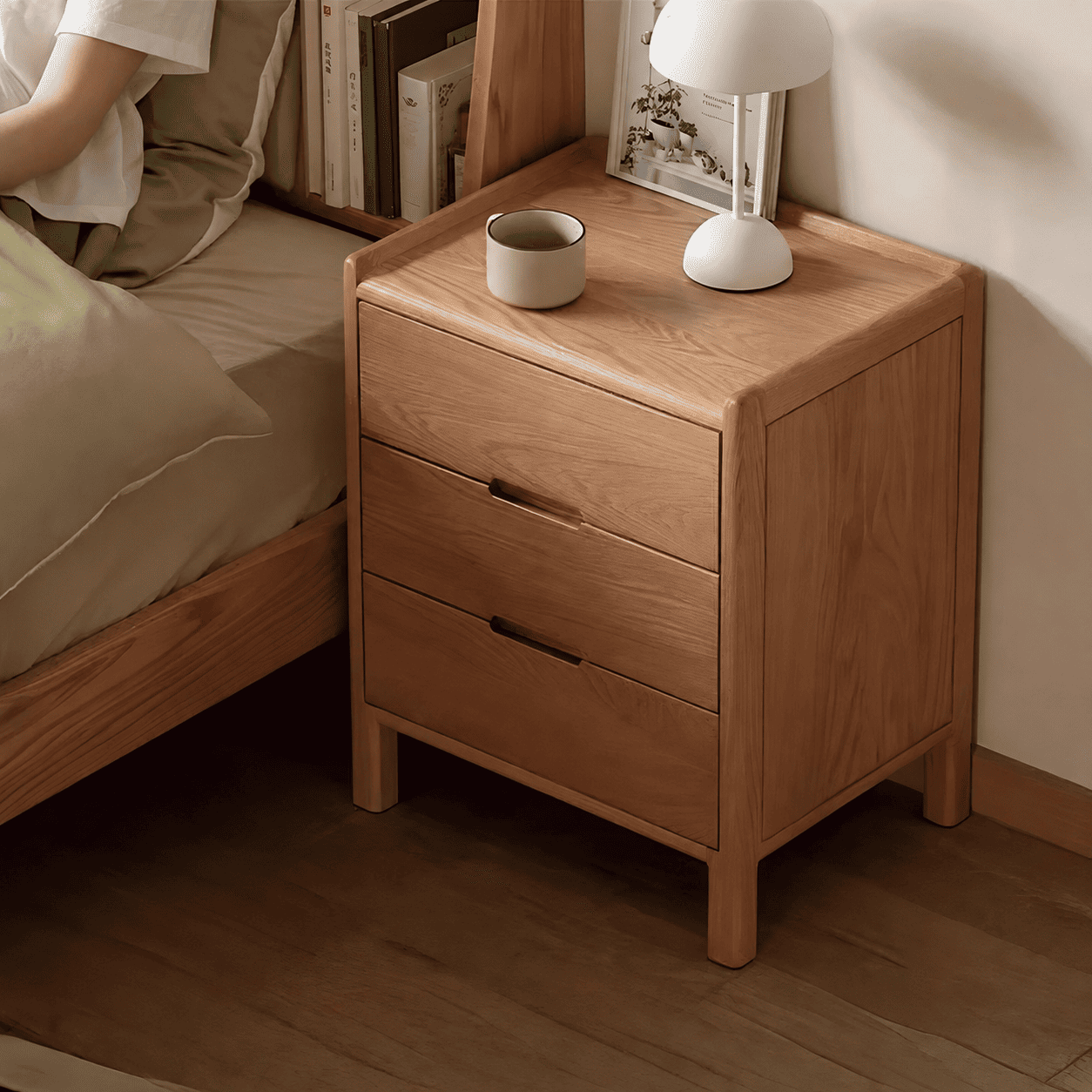 Kusel Natural Solid Oak Bedside Table in a cosy bedroom setting with white table lamp, cup and books on the natural oak top.