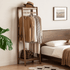 Lahti natural solid walnut narrow coat rack styled beside a wooden bed with hanging clothes