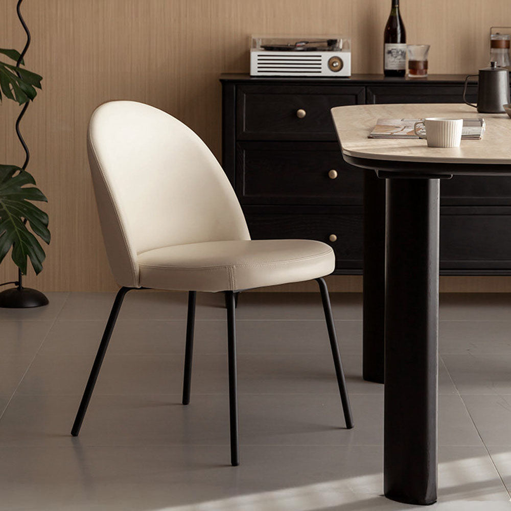 Loreto faux leather dining chair with curved backrest and matte black metal legs, shown in warm white/light brown upholstery.
