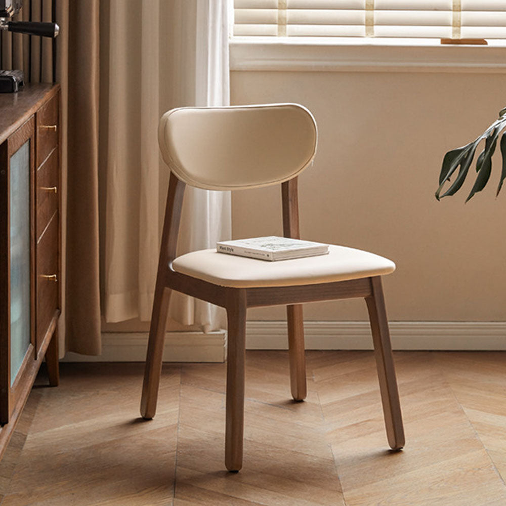 Marche solid walnut dining chair with warm white vegan leather cushion, shown beside a dining table in a bright modern dining space.