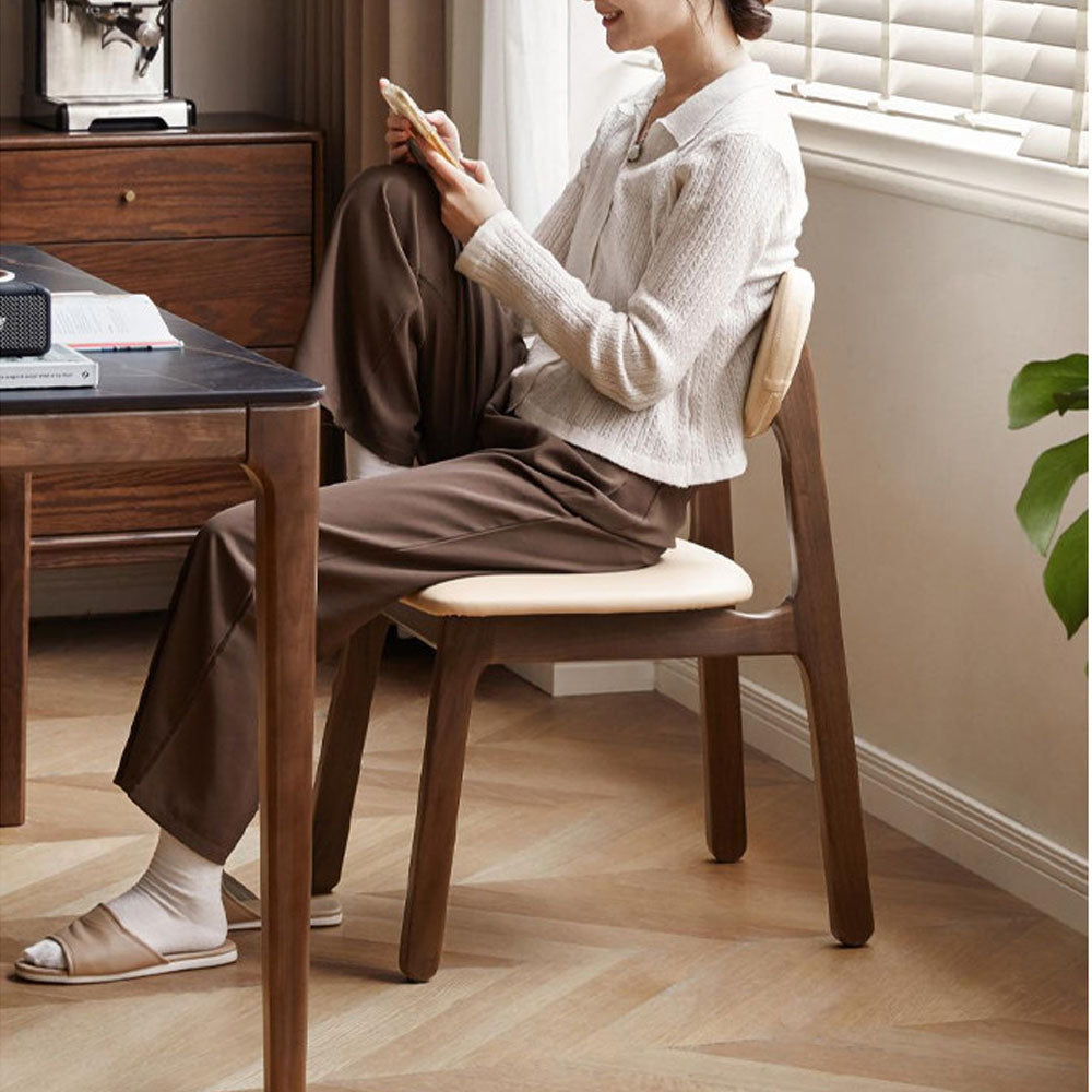 Marche solid walnut dining chair with warm white vegan leather cushion, shown beside a dining table in a bright modern dining space.