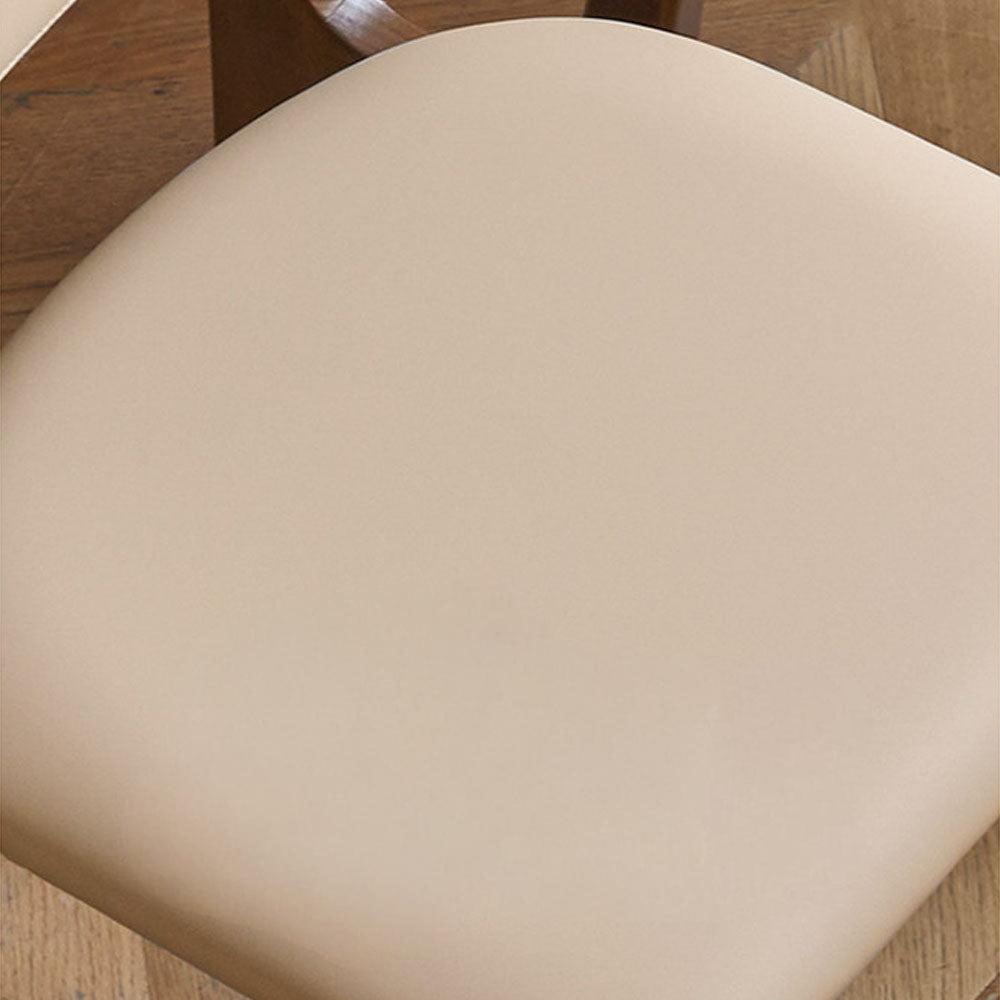 Marche solid walnut dining chair with warm white vegan leather cushion, shown beside a dining table in a bright modern dining space.