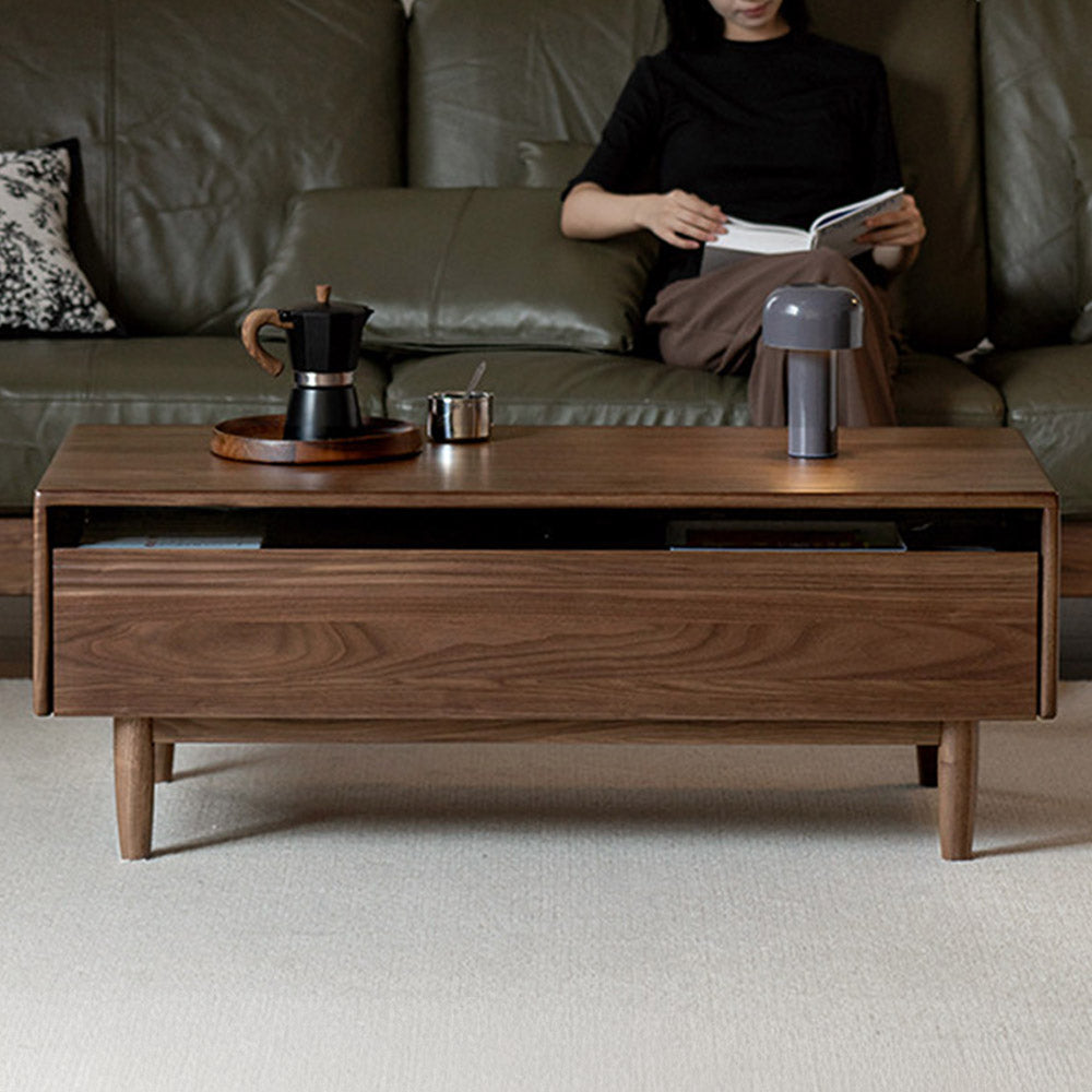 Modena natural solid walnut coffee table with glass-accented drawers and elevated legs in a modern living room setting