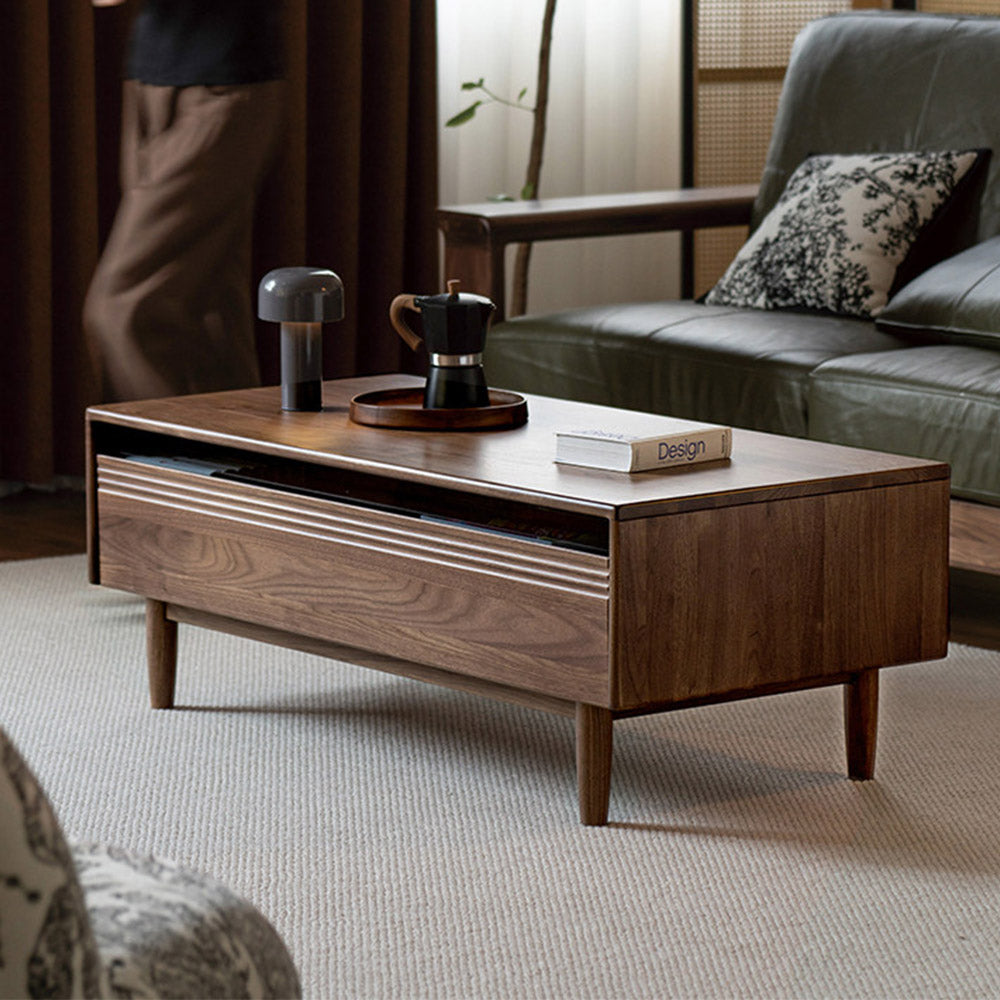 Modena natural solid walnut coffee table with glass-accented drawers and elevated legs in a modern living room setting