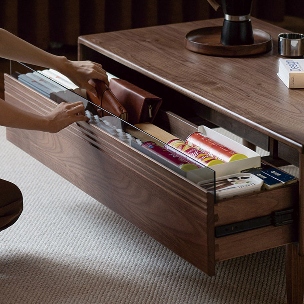 Modena natural solid walnut coffee table with glass-accented drawers and elevated legs in a modern living room setting