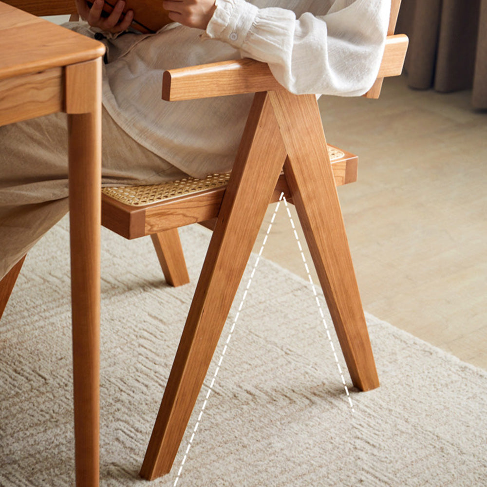 Nordic solid cherry designer chair with woven Indonesian rattan seat and backrest, featuring timber armrests and an angled frame in a sunlit room.