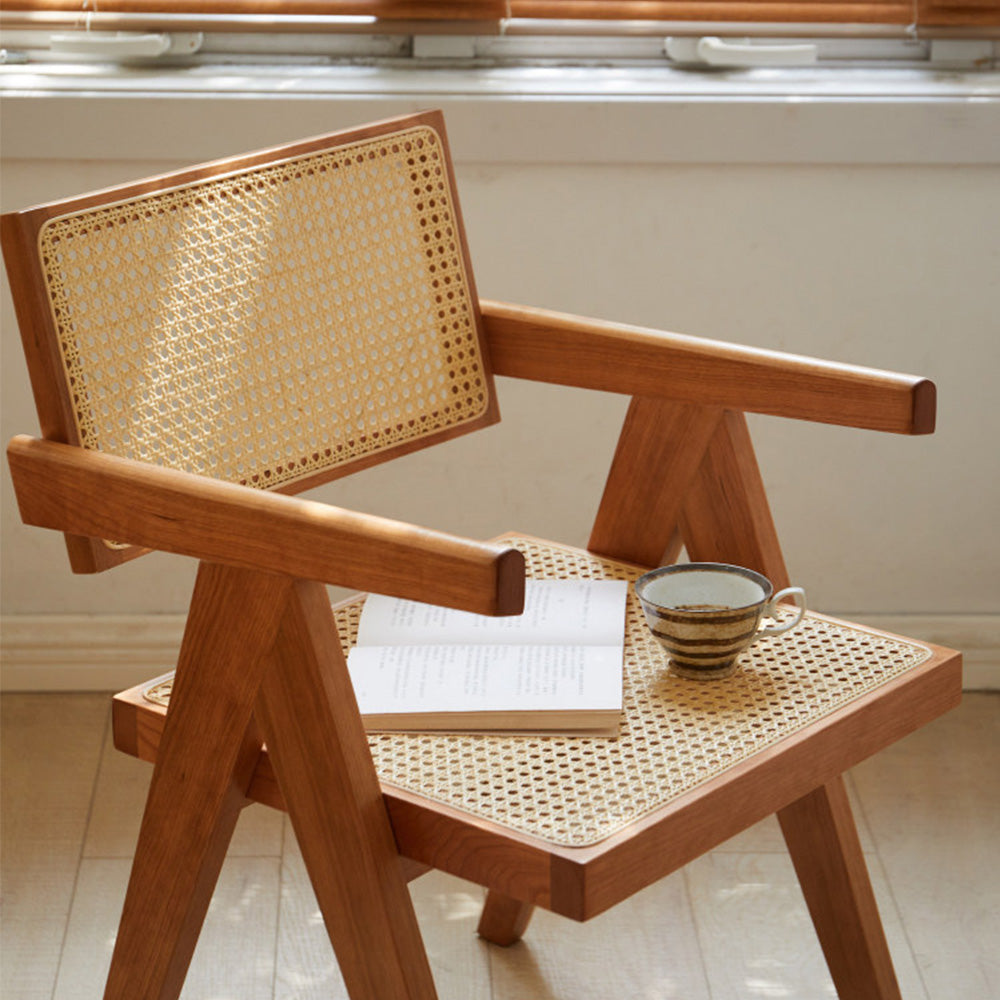 Nordic solid cherry designer chair with woven Indonesian rattan seat and backrest, featuring timber armrests and an angled frame in a sunlit room.