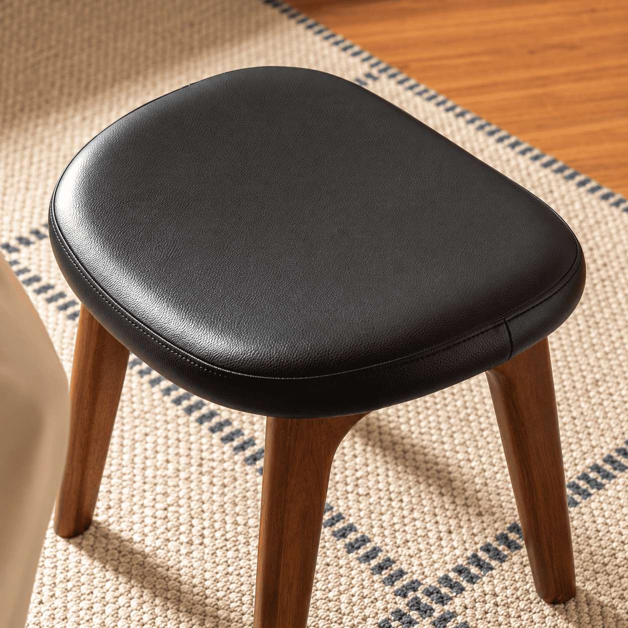 Close up of Norman black upholstered dressing stool seat with rounded cushion edge and walnut legs