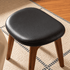 Close up of Norman black upholstered dressing stool seat with rounded cushion edge and walnut legs