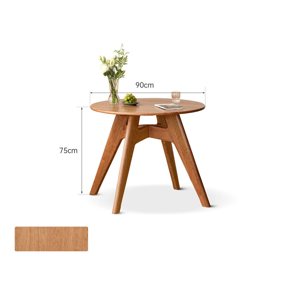 Natural solid cherry small round dining table in a warm timber finish, shown in a compact dining space with dining chairs and kitchen backdrop