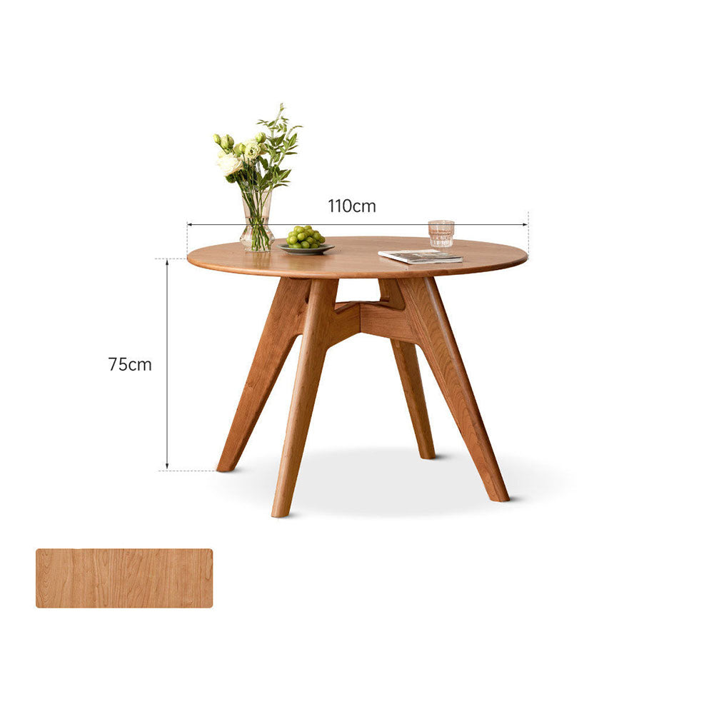 Natural solid cherry small round dining table in a warm timber finish, shown in a compact dining space with dining chairs and kitchen backdrop
