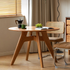 Natural solid cherry small round dining table in a warm timber finish, shown in a compact dining space with dining chairs and kitchen backdrop