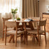 Natural solid cherry small round dining table in a warm timber finish, shown in a compact dining space with dining chairs and kitchen backdrop