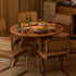 Natural solid cherry small round dining table in a warm timber finish, shown in a compact dining space with dining chairs and kitchen backdrop