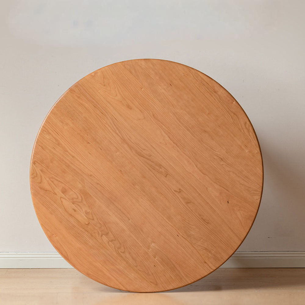 Natural solid cherry small round dining table in a warm timber finish, shown in a compact dining space with dining chairs and kitchen backdrop