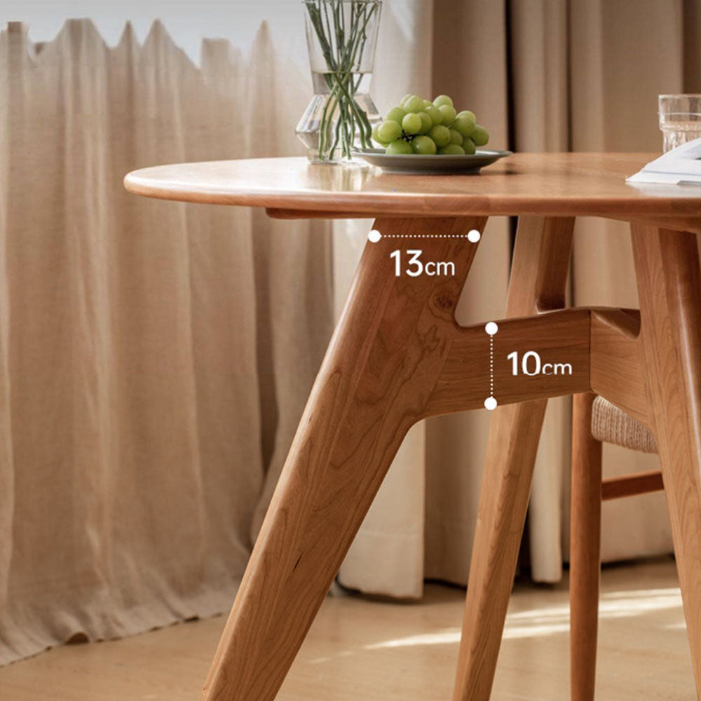 Natural solid cherry small round dining table in a warm timber finish, shown in a compact dining space with dining chairs and kitchen backdrop