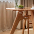 Natural solid cherry small round dining table in a warm timber finish, shown in a compact dining space with dining chairs and kitchen backdrop