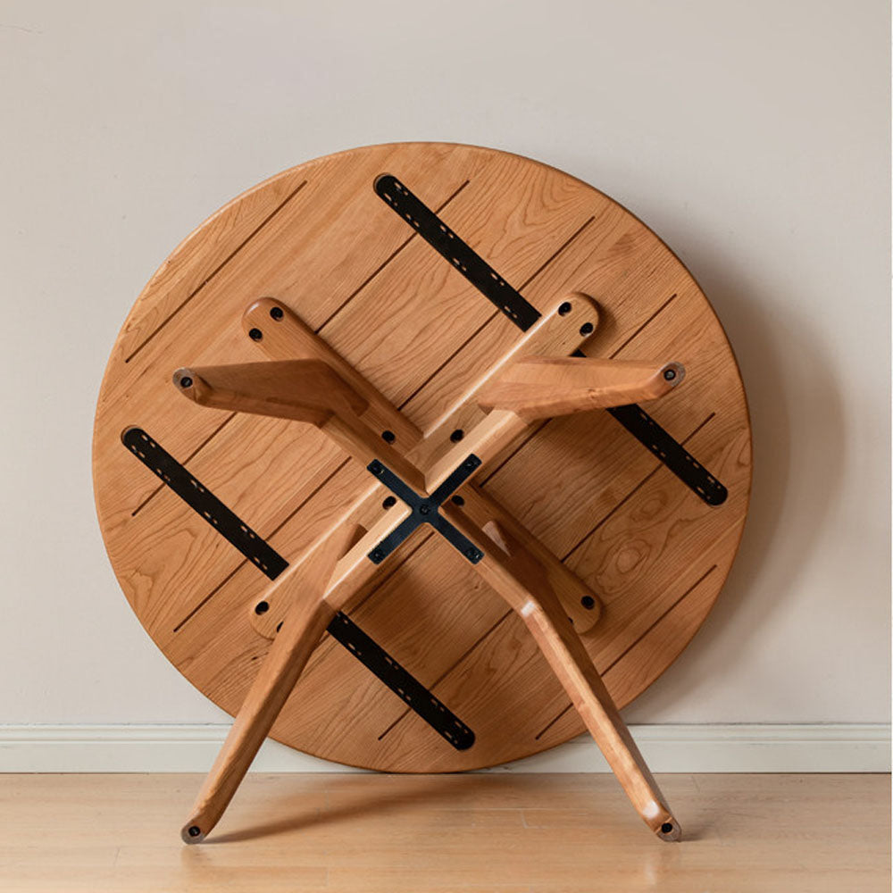 Natural solid cherry small round dining table in a warm timber finish, shown in a compact dining space with dining chairs and kitchen backdrop