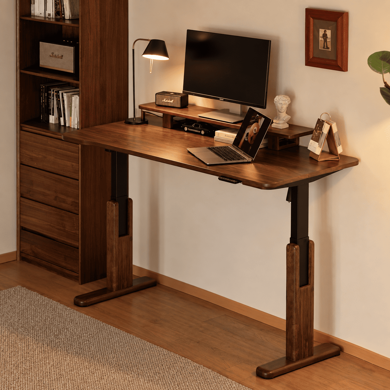 Prunus walnut electric height adjustable desk shown in a warm home office setting with monitor and laptop
