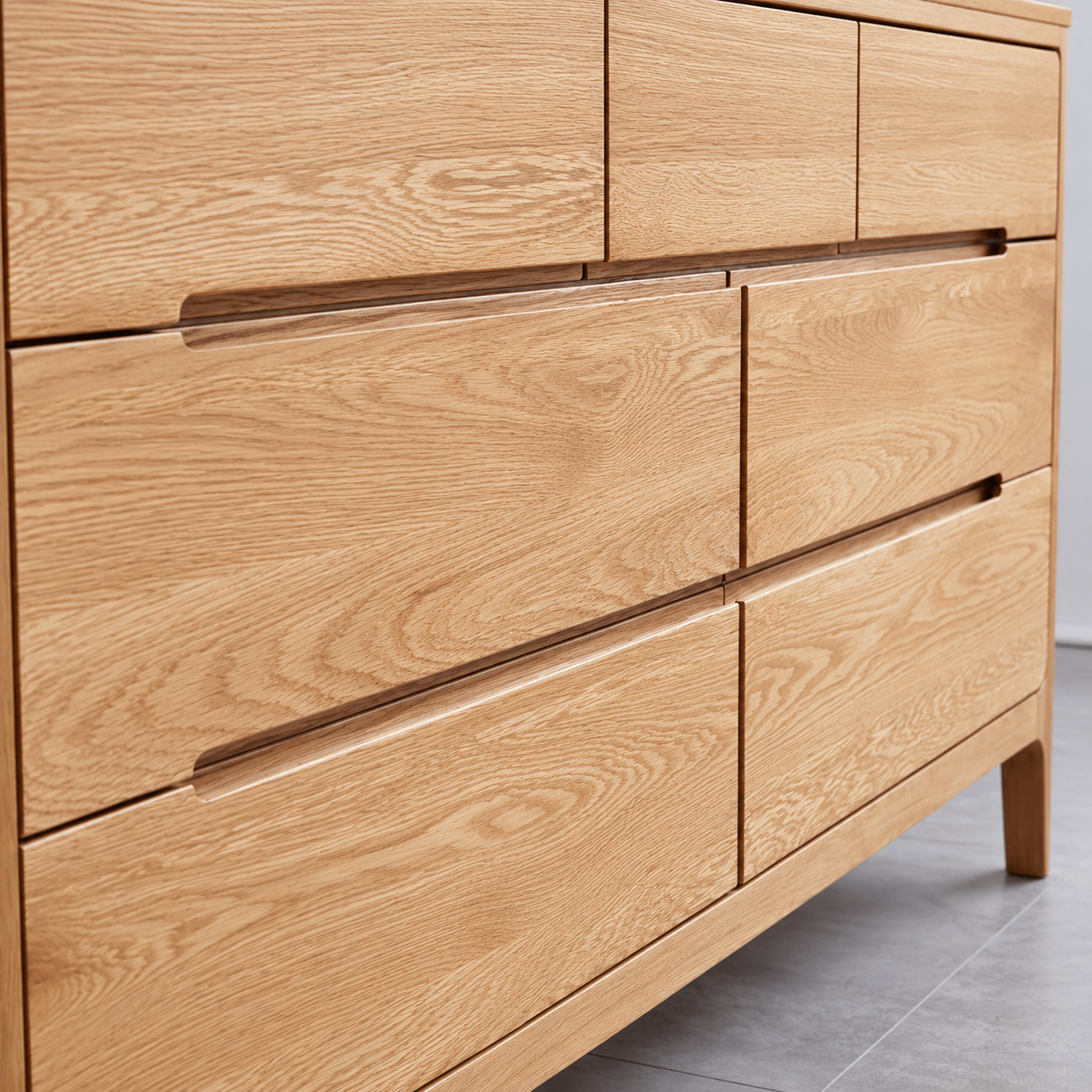 Close-up of a light oak wood dresser with six drawers and minimalist linear handles, set against a neutral gray tiled floor.