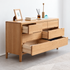 A light oak wood dresser with six drawers, some open, styled with books, a picture frame, and decorative items on top, set against a neutral light gray wall and floor.