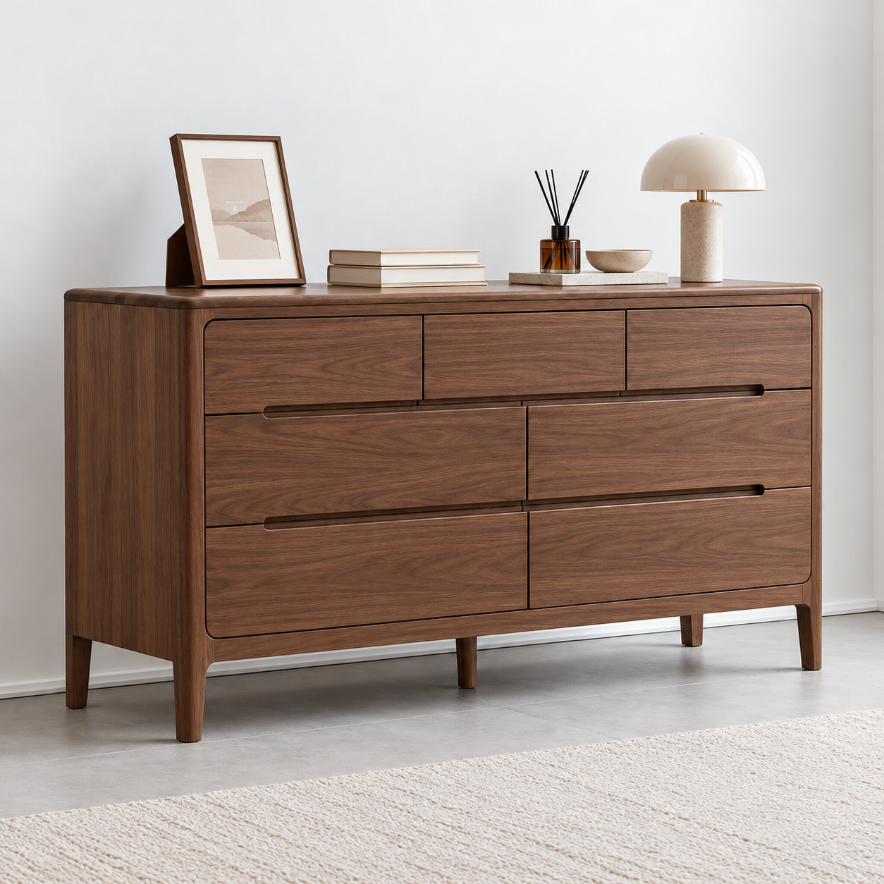 A mid-century modern wooden dresser with six drawers, styled with books, a lamp, a bowl, and a picture frame in a minimalist room.